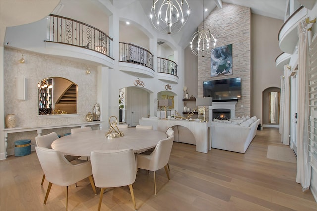 dining space featuring high vaulted ceiling, a fireplace, an inviting chandelier, and light hardwood / wood-style floors