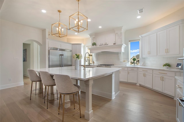 kitchen featuring sink, white cabinetry, hanging light fixtures, a center island with sink, and stainless steel built in fridge