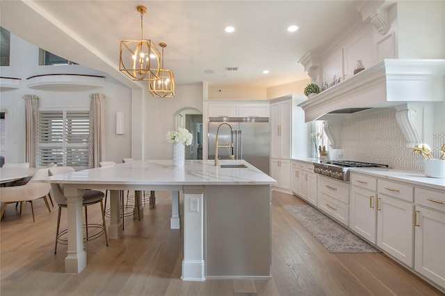 kitchen featuring a breakfast bar area, decorative light fixtures, a center island with sink, stainless steel appliances, and light stone countertops