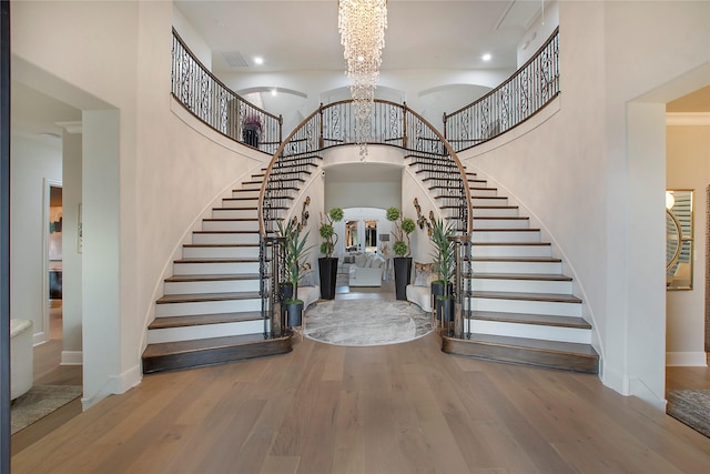 entryway featuring wood-type flooring, a towering ceiling, and a notable chandelier