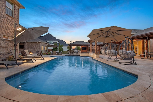 pool at dusk with a gazebo, a patio, and pool water feature