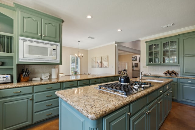 kitchen with stainless steel gas stovetop, white microwave, sink, an island with sink, and a notable chandelier