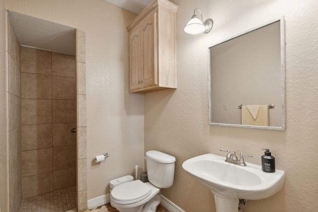 bathroom with tiled shower, toilet, and sink