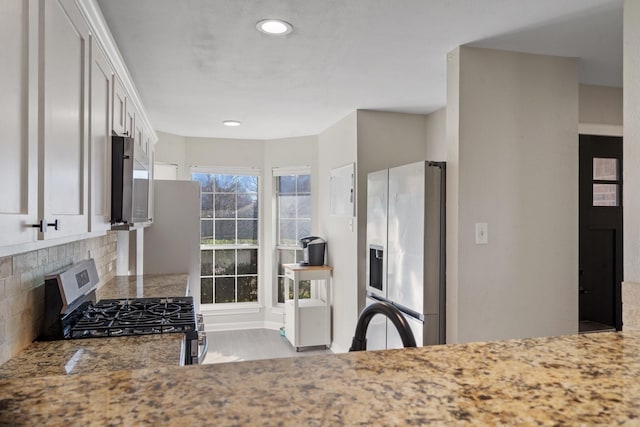 kitchen featuring stone countertops, backsplash, white cabinets, and appliances with stainless steel finishes