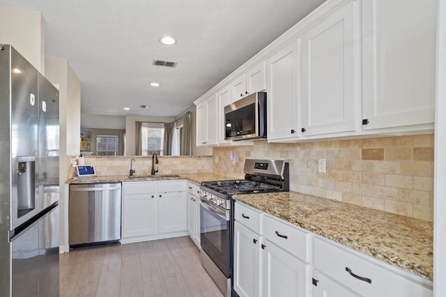 kitchen featuring sink, white cabinetry, stainless steel appliances, light stone countertops, and decorative backsplash