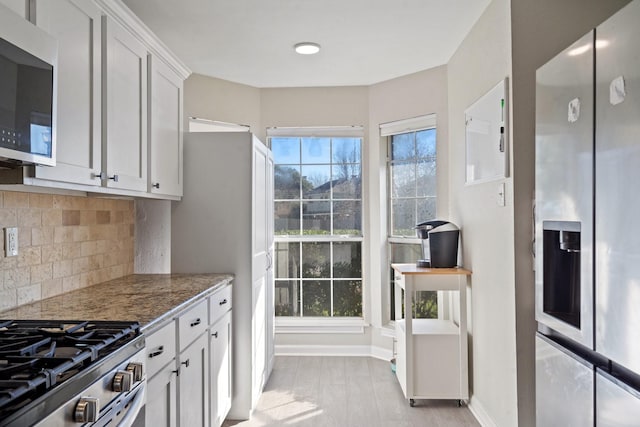 kitchen featuring appliances with stainless steel finishes, white cabinetry, tasteful backsplash, light hardwood / wood-style floors, and dark stone counters