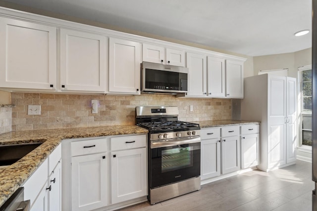 kitchen with white cabinetry, appliances with stainless steel finishes, backsplash, and light stone counters