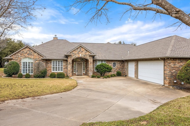 view of front of house with driveway, roof with shingles, a front yard, a garage, and a chimney