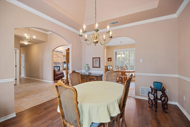 dining space featuring an inviting chandelier, crown molding, a tray ceiling, a fireplace, and hardwood / wood-style flooring