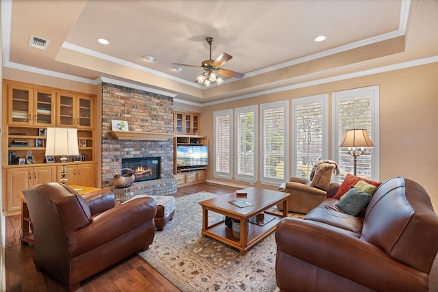 living room with a fireplace, a tray ceiling, hardwood / wood-style flooring, and ceiling fan