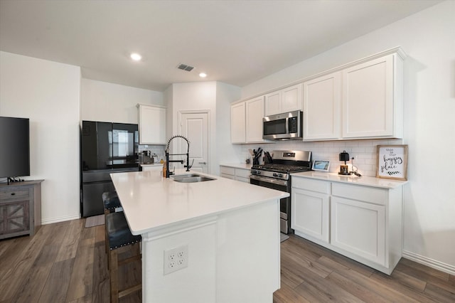 kitchen with sink, white cabinetry, light wood-type flooring, appliances with stainless steel finishes, and an island with sink