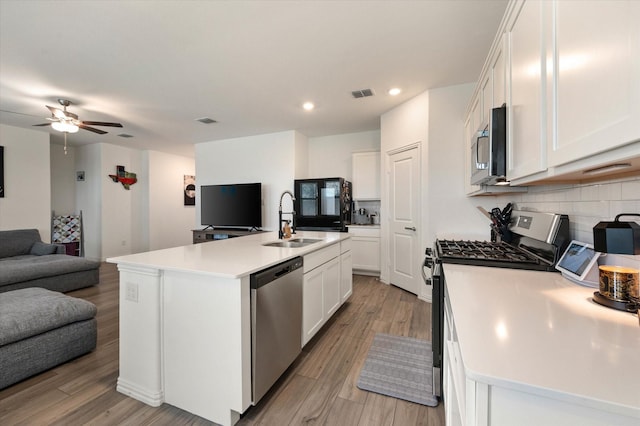 kitchen with white cabinetry, sink, stainless steel appliances, a center island with sink, and light hardwood / wood-style flooring