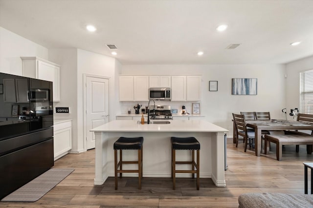 kitchen featuring stainless steel appliances, white cabinetry, a kitchen island with sink, and sink