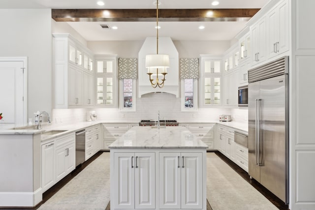 kitchen featuring a kitchen island with sink, white cabinets, beamed ceiling, and built in appliances