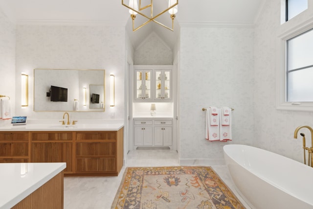 full bathroom featuring two vanities, a sink, a freestanding bath, ornamental molding, and wallpapered walls