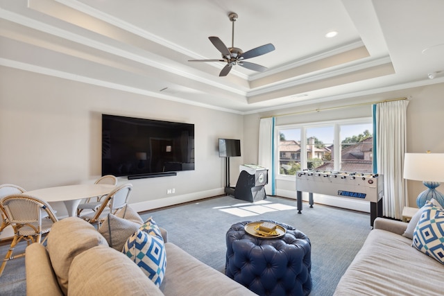 carpeted living room featuring a ceiling fan, baseboards, a tray ceiling, and crown molding