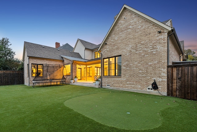 back of property featuring brick siding, fence, a yard, a trampoline, and a chimney