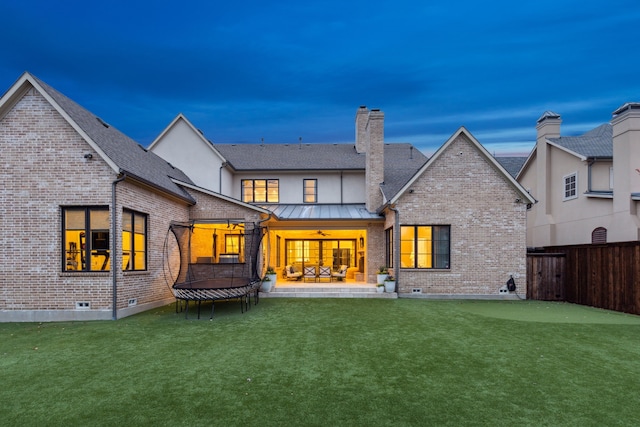 back of house with ceiling fan, a standing seam roof, a trampoline, a patio area, and brick siding