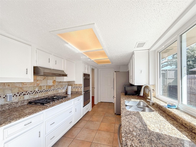 kitchen featuring sink, light tile patterned floors, dark stone counters, white cabinets, and appliances with stainless steel finishes