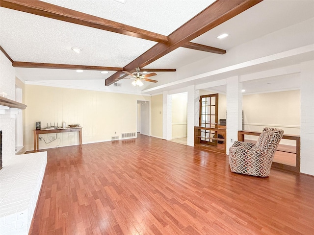 unfurnished living room featuring hardwood / wood-style flooring, ceiling fan, beam ceiling, a textured ceiling, and a brick fireplace