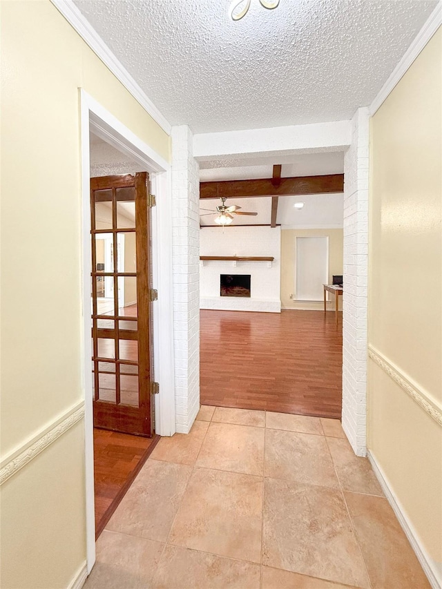 hall featuring beamed ceiling, light tile patterned floors, a textured ceiling, and ornamental molding