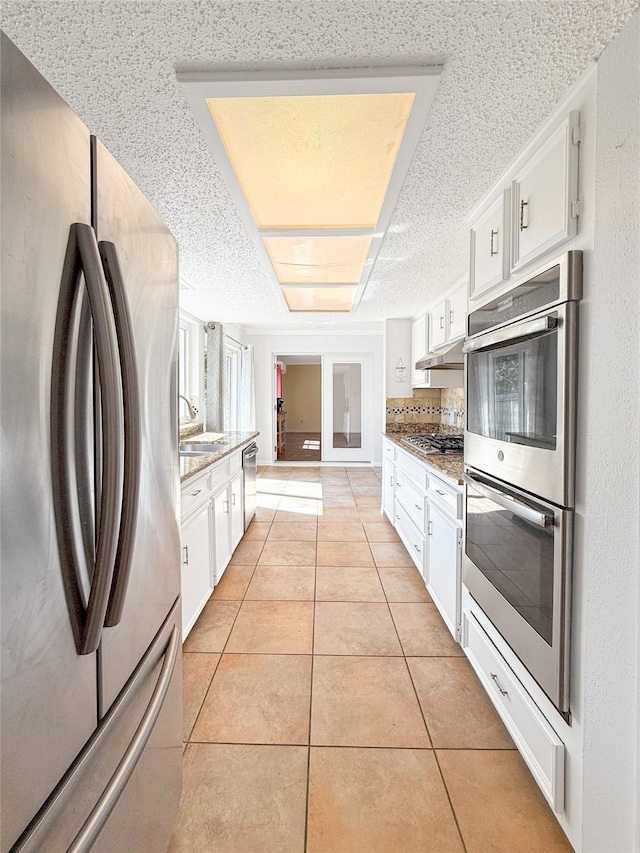 kitchen featuring white cabinetry, light stone countertops, stainless steel appliances, and light tile patterned flooring