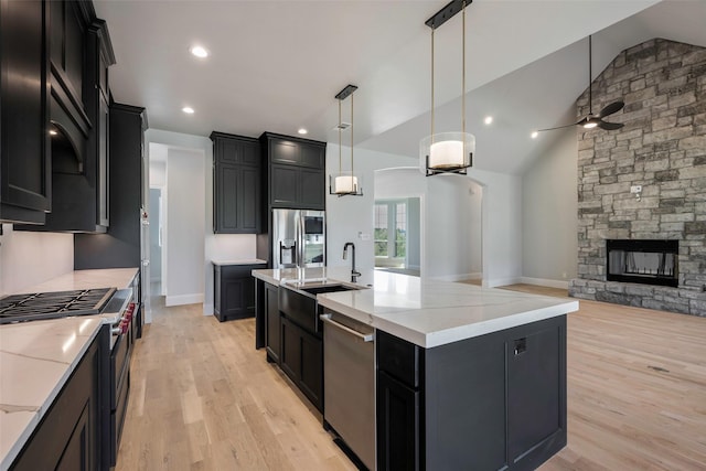 kitchen featuring sink, appliances with stainless steel finishes, hanging light fixtures, a center island with sink, and a stone fireplace