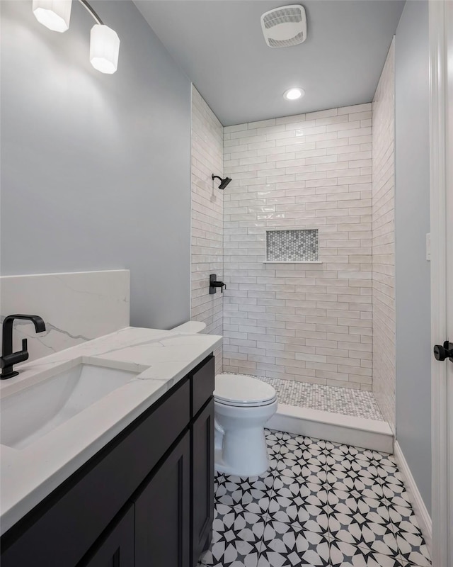 bathroom with tiled shower, vanity, and toilet