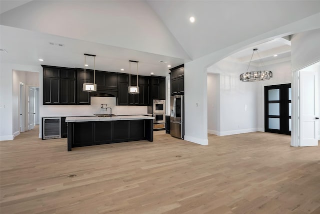 kitchen with light hardwood / wood-style flooring, an island with sink, pendant lighting, stainless steel appliances, and beverage cooler