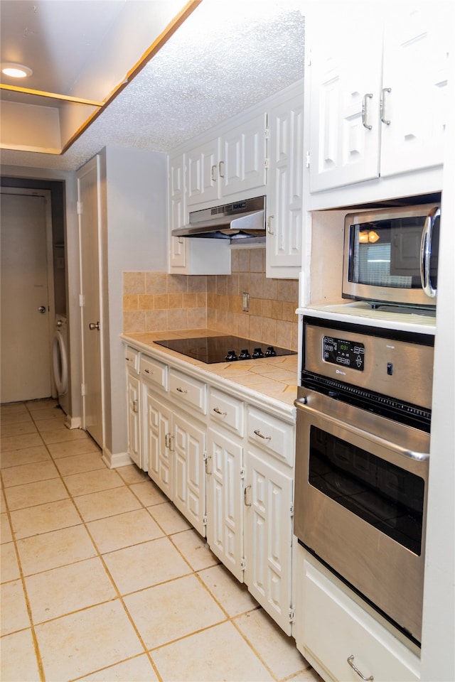 kitchen with appliances with stainless steel finishes, backsplash, light tile patterned floors, washer / clothes dryer, and white cabinetry