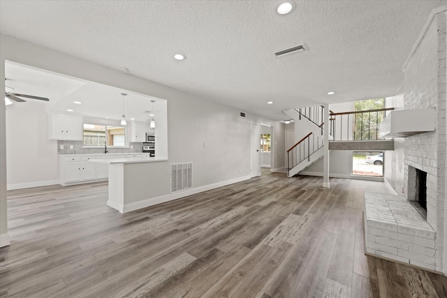 unfurnished living room with ceiling fan, light wood-type flooring, a textured ceiling, and a brick fireplace