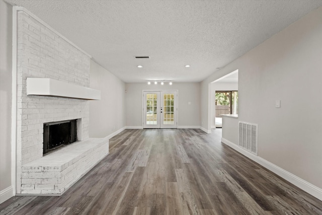 unfurnished living room featuring track lighting, french doors, hardwood / wood-style flooring, a fireplace, and a textured ceiling