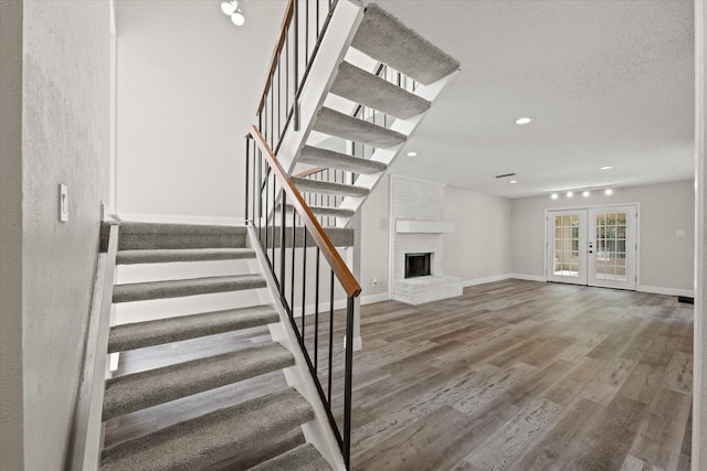 staircase with hardwood / wood-style flooring, a textured ceiling, a fireplace, and french doors