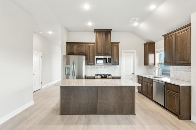 kitchen with light stone counters, lofted ceiling, decorative backsplash, a kitchen island, and appliances with stainless steel finishes