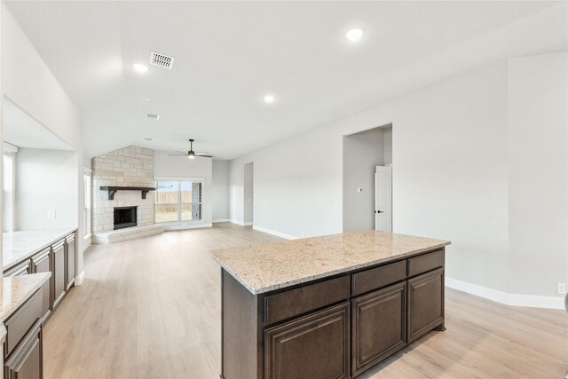 unfurnished living room with ceiling fan, light wood-type flooring, a stone fireplace, and a wealth of natural light