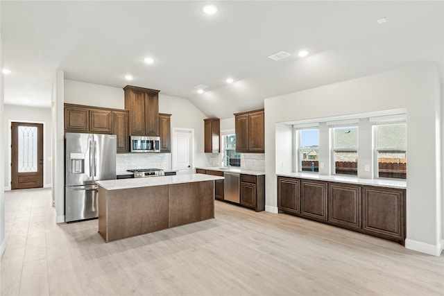 kitchen featuring vaulted ceiling, stainless steel appliances, light wood-type flooring, a kitchen island, and tasteful backsplash