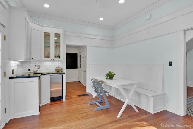 kitchen with a sink, white cabinets, dark countertops, glass insert cabinets, and crown molding