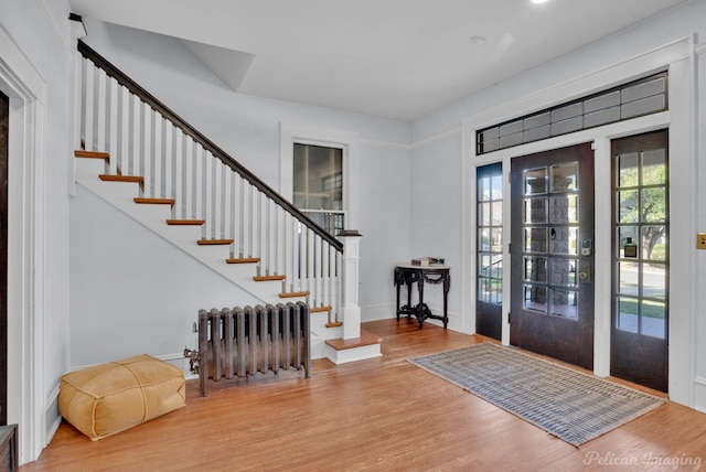 entrance foyer with stairway, radiator heating unit, and wood finished floors