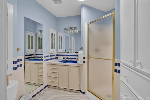 bathroom featuring tile patterned floors, vanity, a shower with shower door, and tile walls