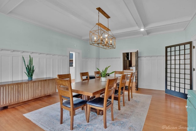 dining space with a wainscoted wall, an inviting chandelier, beam ceiling, and light wood-style floors