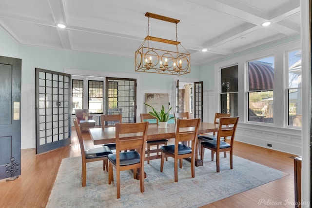 dining room with light wood-style floors, beam ceiling, coffered ceiling, and a decorative wall