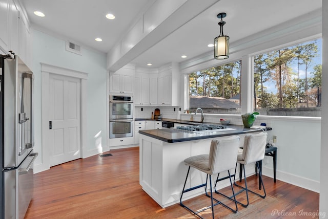 kitchen with a breakfast bar area, stainless steel appliances, white cabinets, dark countertops, and decorative light fixtures