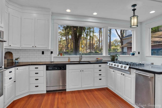 kitchen with decorative light fixtures, dark countertops, appliances with stainless steel finishes, white cabinets, and a sink