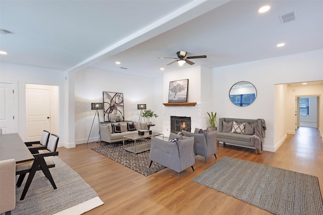 living room featuring ceiling fan, a stone fireplace, and light wood-type flooring