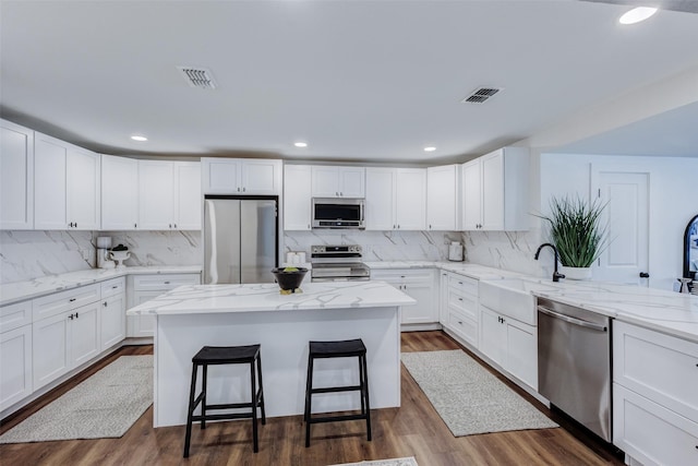 kitchen featuring white cabinetry, sink, stainless steel appliances, a kitchen bar, and a kitchen island