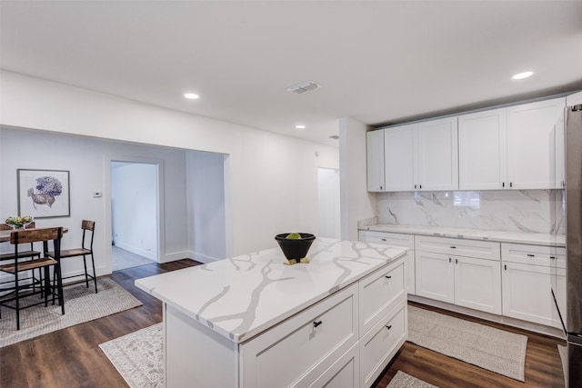 kitchen featuring white cabinetry, a center island, light stone countertops, dark hardwood / wood-style flooring, and backsplash