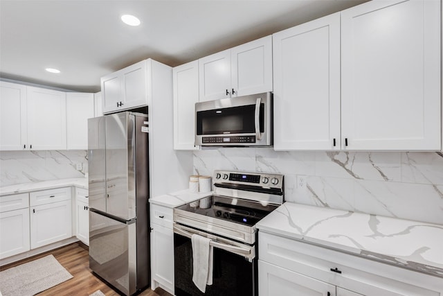 kitchen with white cabinets, backsplash, light wood-type flooring, and stainless steel appliances