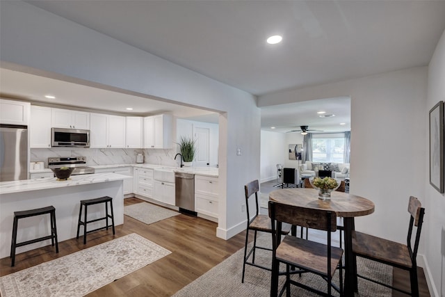 kitchen featuring a breakfast bar, tasteful backsplash, dark hardwood / wood-style flooring, white cabinetry, and stainless steel appliances