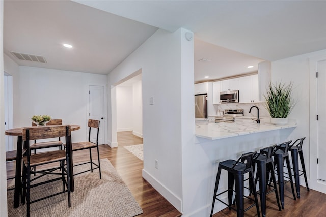 kitchen with white cabinetry, stainless steel appliances, tasteful backsplash, dark hardwood / wood-style floors, and kitchen peninsula