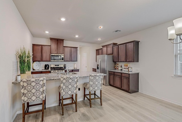 kitchen featuring light stone countertops, a kitchen bar, stainless steel appliances, backsplash, and light hardwood / wood-style flooring